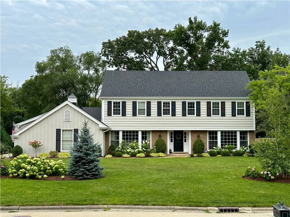 Two-story white colonial home with a dark shingle roof and a landscaped front lawn